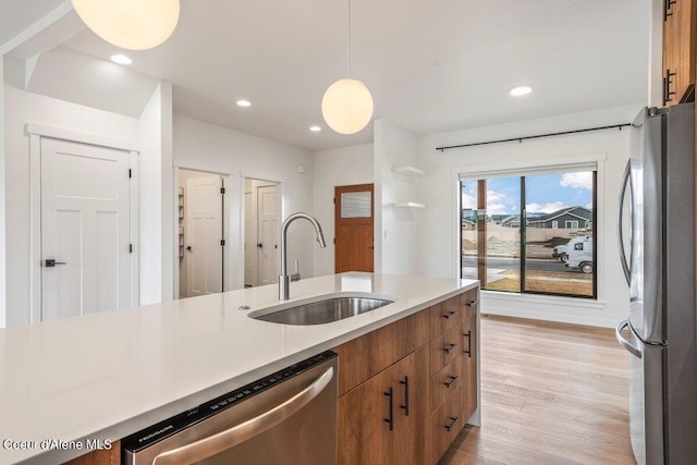 kitchen featuring appliances with stainless steel finishes, light wood-type flooring, hanging light fixtures, and sink