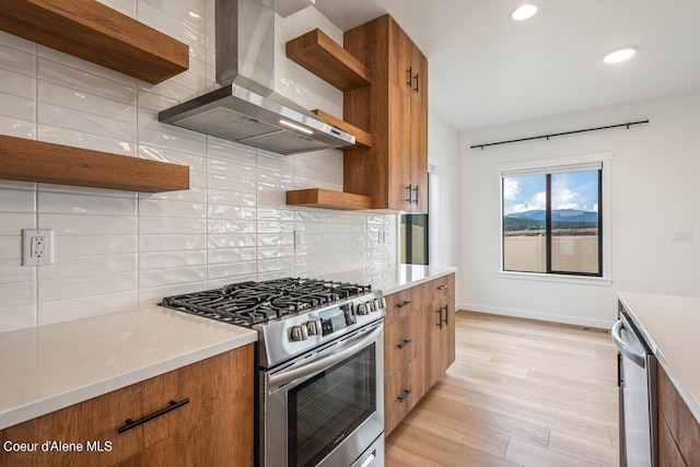 kitchen with backsplash, stainless steel appliances, light hardwood / wood-style flooring, and wall chimney range hood