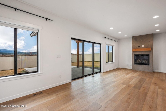 unfurnished living room featuring a fireplace, light wood-type flooring, and a wealth of natural light