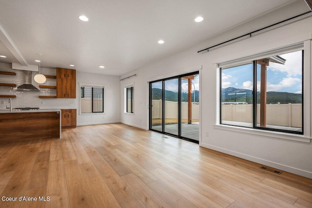 unfurnished living room featuring a mountain view, a healthy amount of sunlight, and light hardwood / wood-style flooring