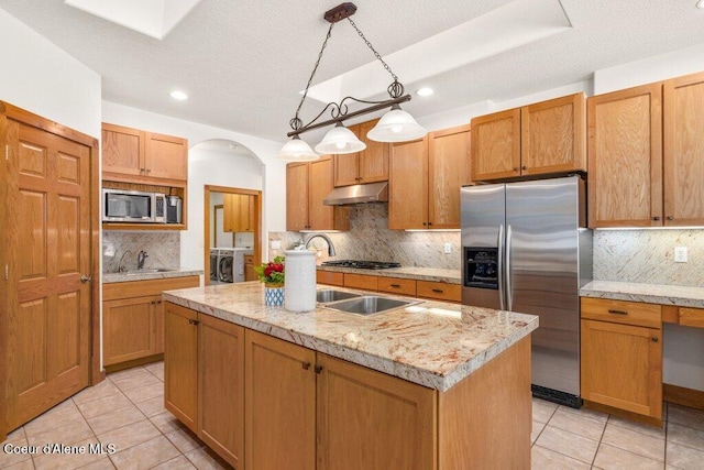 kitchen with washer and clothes dryer, decorative light fixtures, an island with sink, tasteful backsplash, and appliances with stainless steel finishes