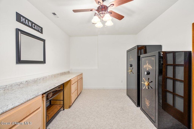 kitchen with ceiling fan, light carpet, built in desk, and light brown cabinets