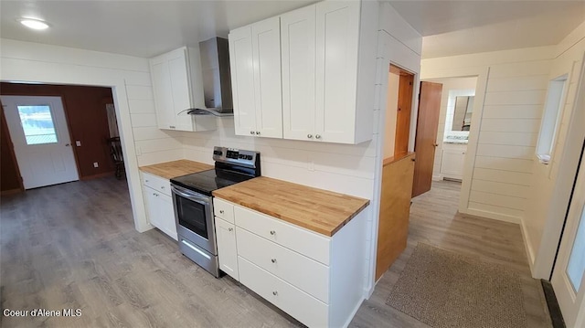 kitchen with wall chimney range hood, white cabinetry, stainless steel range with electric stovetop, and wood counters