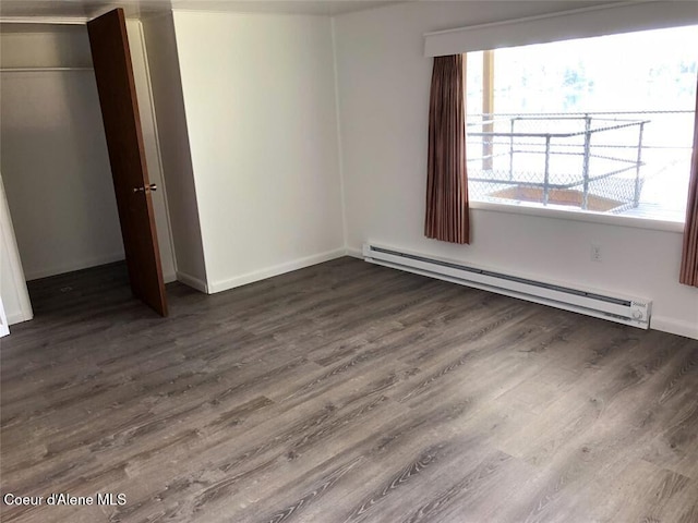 unfurnished bedroom featuring dark hardwood / wood-style flooring, multiple windows, baseboard heating, and a closet