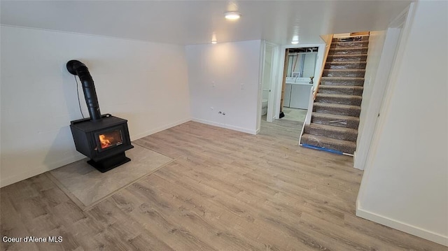 unfurnished living room featuring a wood stove, light hardwood / wood-style flooring, and washer / dryer