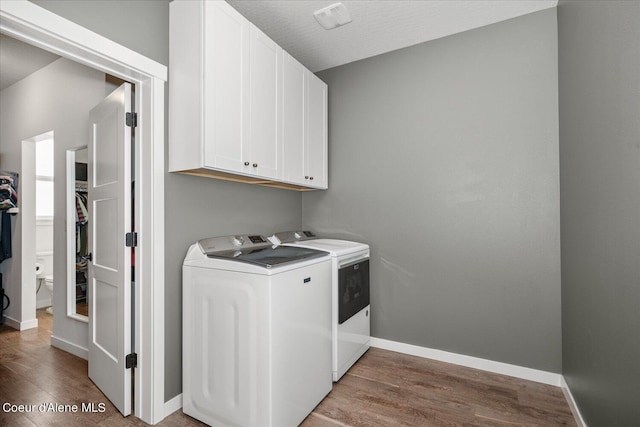 clothes washing area featuring washing machine and clothes dryer, cabinets, a textured ceiling, and hardwood / wood-style flooring