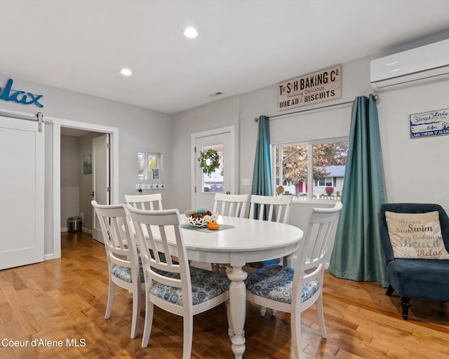 dining space with a wall unit AC, a barn door, and light hardwood / wood-style flooring