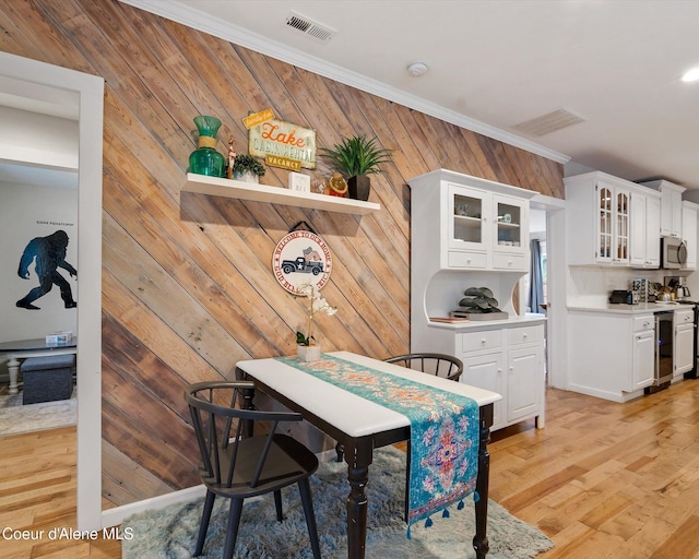 dining area with crown molding, wooden walls, and light hardwood / wood-style flooring