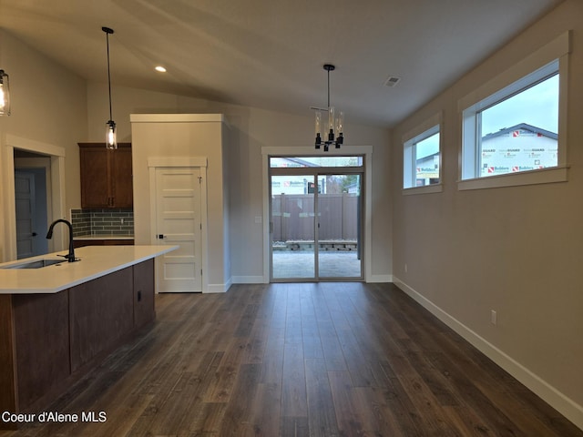 kitchen featuring pendant lighting, lofted ceiling, backsplash, sink, and a chandelier