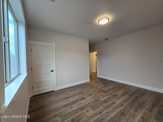 spare room with a textured ceiling, a wealth of natural light, and dark wood-type flooring