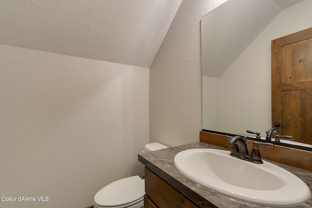 bathroom with vanity, toilet, a textured ceiling, and vaulted ceiling