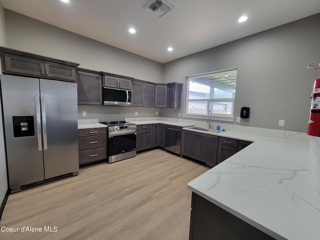 kitchen featuring sink, light stone counters, dark brown cabinetry, stainless steel appliances, and light wood-type flooring