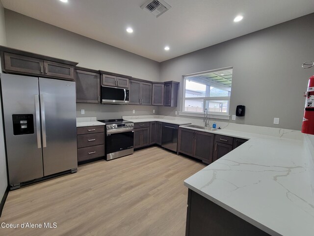 kitchen featuring light stone counters, stainless steel appliances, visible vents, light wood-style floors, and a sink