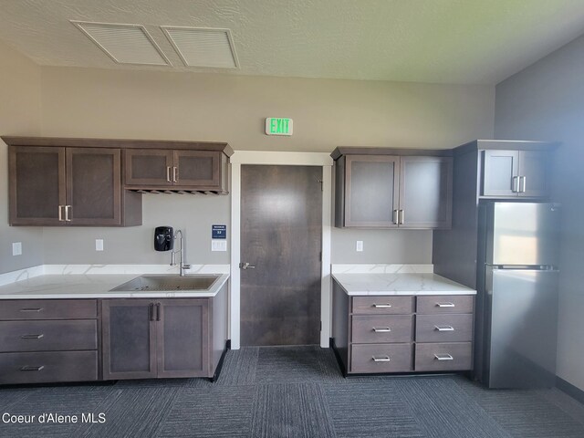 kitchen featuring dark brown cabinetry, visible vents, light stone counters, freestanding refrigerator, and a sink