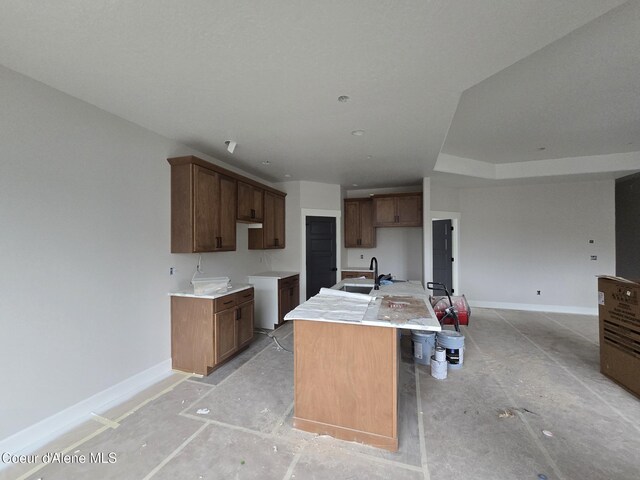 kitchen featuring light countertops, an island with sink, a sink, and baseboards