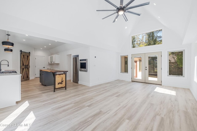 unfurnished living room with high vaulted ceiling, french doors, sink, ceiling fan, and a barn door