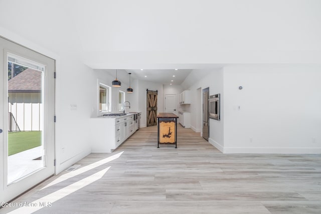 kitchen with lofted ceiling, white cabinets, hanging light fixtures, light hardwood / wood-style floors, and stainless steel appliances