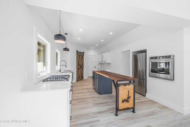 kitchen featuring a breakfast bar, white cabinets, a barn door, appliances with stainless steel finishes, and decorative light fixtures