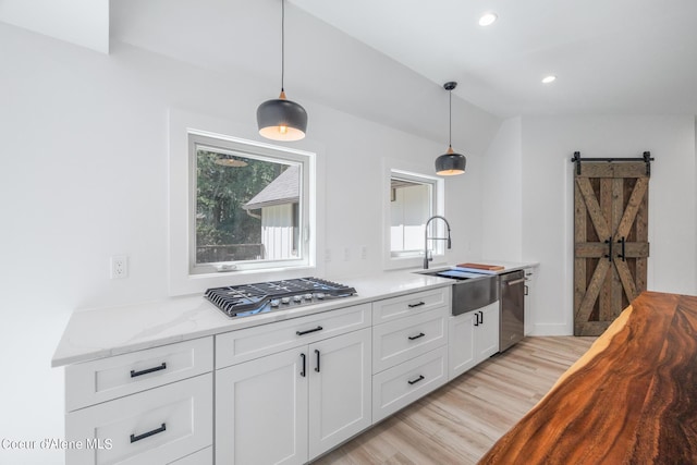 kitchen with light stone countertops, stainless steel appliances, sink, a barn door, and white cabinetry