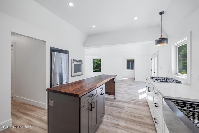 kitchen with lofted ceiling, butcher block countertops, decorative light fixtures, white cabinetry, and stainless steel appliances