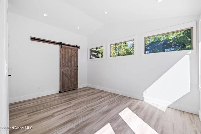 spare room featuring a barn door, light hardwood / wood-style floors, and lofted ceiling