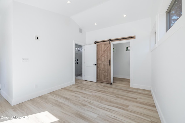 unfurnished bedroom with a barn door, light hardwood / wood-style flooring, and lofted ceiling