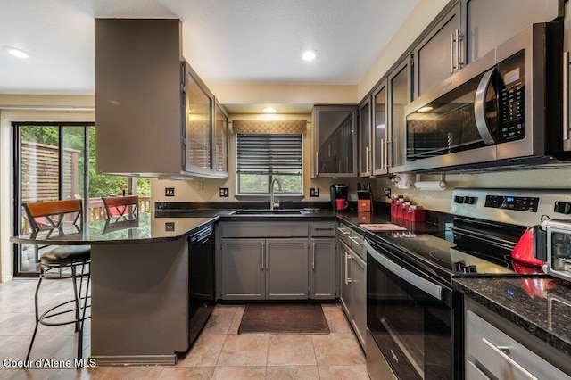 kitchen with a breakfast bar area, dark stone counters, appliances with stainless steel finishes, and sink