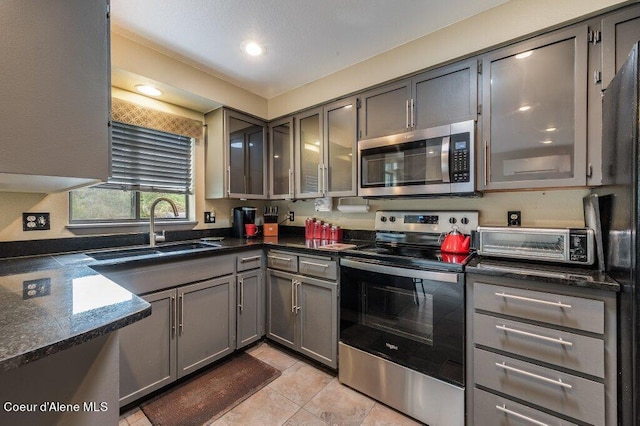 kitchen with appliances with stainless steel finishes, sink, gray cabinetry, light tile patterned floors, and dark stone countertops