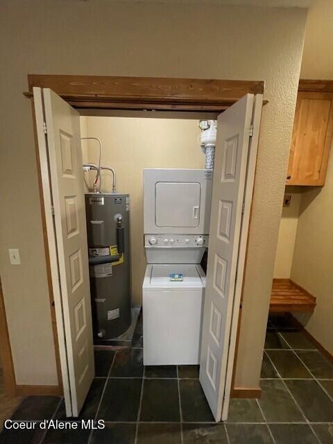 washroom with electric water heater and stacked washer / dryer