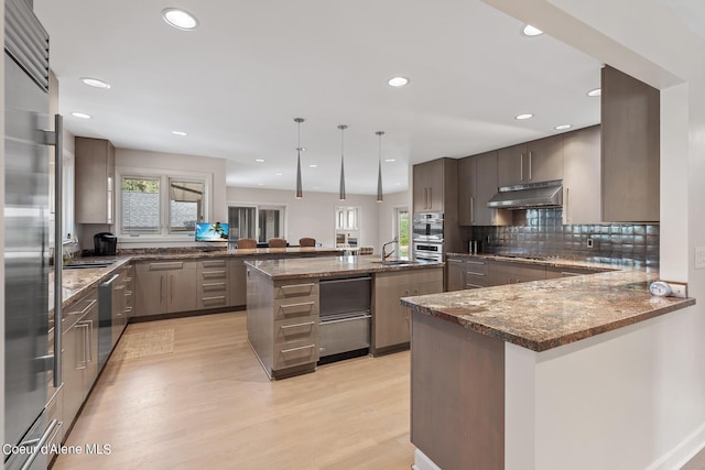 kitchen with sink, dark stone countertops, decorative light fixtures, light hardwood / wood-style floors, and kitchen peninsula