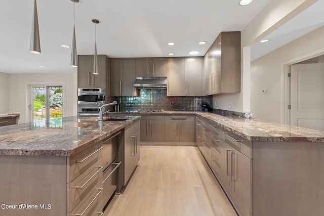 kitchen with sink, tasteful backsplash, dark stone counters, light hardwood / wood-style floors, and decorative light fixtures