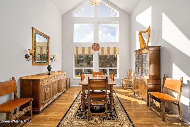 dining space with baseboards, light wood-style floors, and high vaulted ceiling