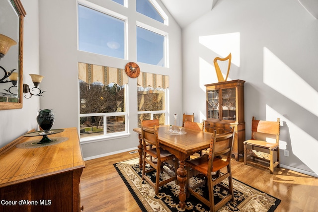 dining room with high vaulted ceiling, baseboards, and wood finished floors