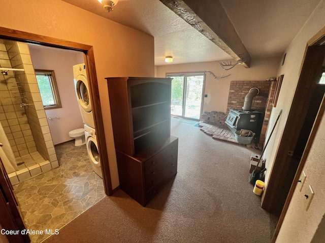 bathroom with a wood stove, a textured ceiling, toilet, walk in shower, and stacked washer / drying machine