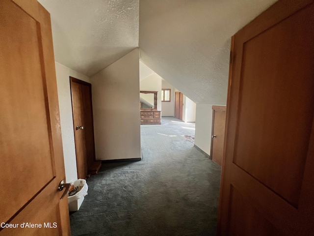 corridor featuring a textured ceiling, vaulted ceiling, and dark carpet