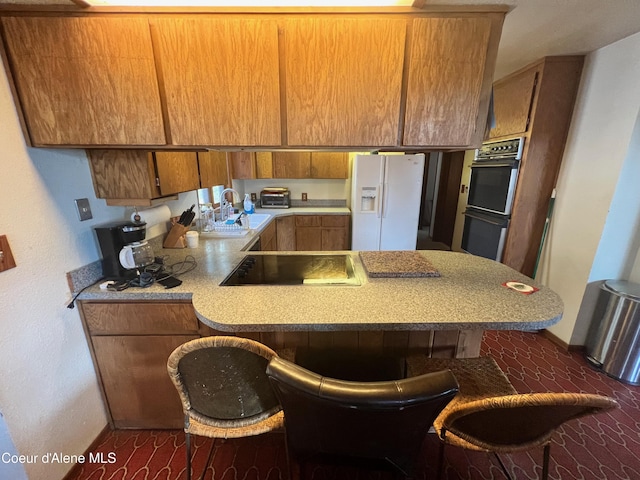 kitchen featuring black electric stovetop, a kitchen bar, white refrigerator with ice dispenser, and sink