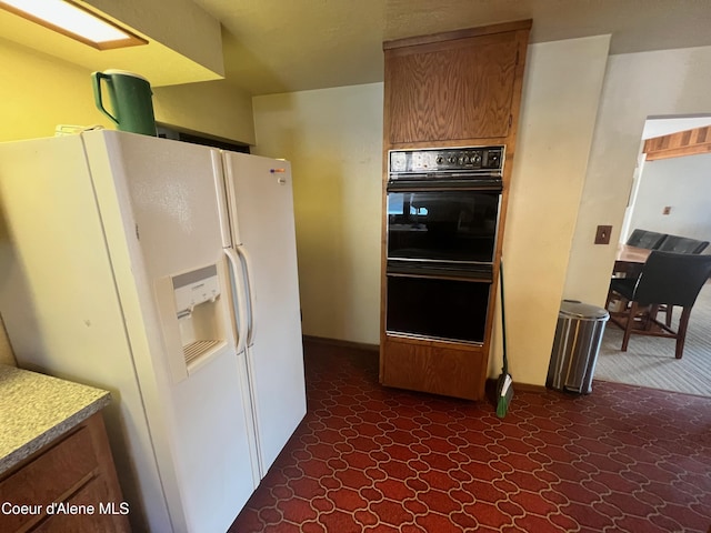 kitchen with black double oven and white refrigerator with ice dispenser