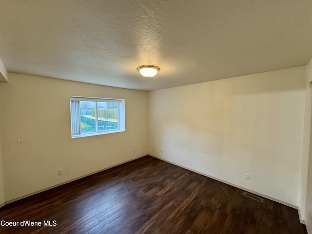 empty room with dark hardwood / wood-style flooring and a textured ceiling