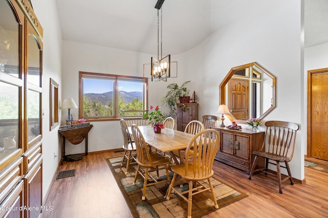 dining area with a mountain view, a towering ceiling, light wood-type flooring, and a notable chandelier