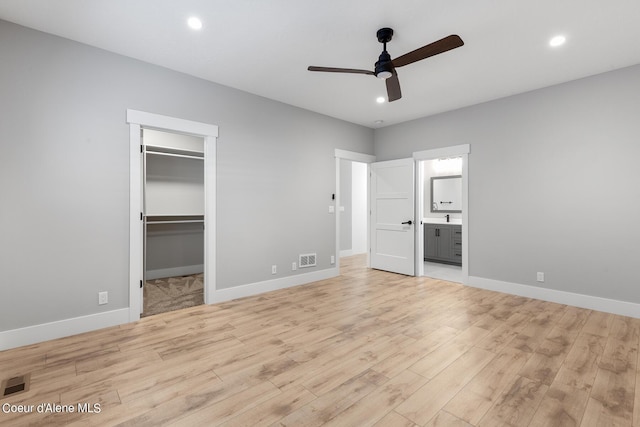 unfurnished bedroom featuring ensuite bath, a spacious closet, ceiling fan, a closet, and light wood-type flooring