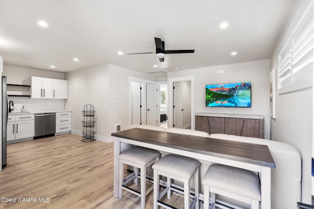 kitchen featuring decorative backsplash, light wood-type flooring, stainless steel dishwasher, a breakfast bar, and white cabinetry