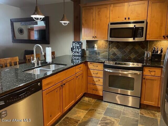 kitchen featuring backsplash, sink, hanging light fixtures, dark stone countertops, and appliances with stainless steel finishes