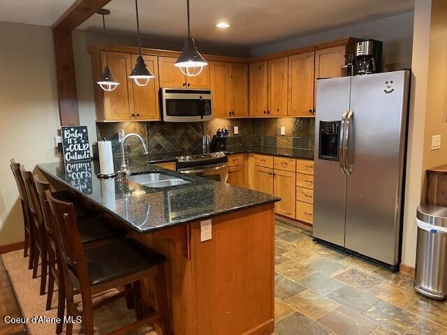 kitchen featuring sink, stainless steel appliances, tasteful backsplash, dark stone countertops, and pendant lighting