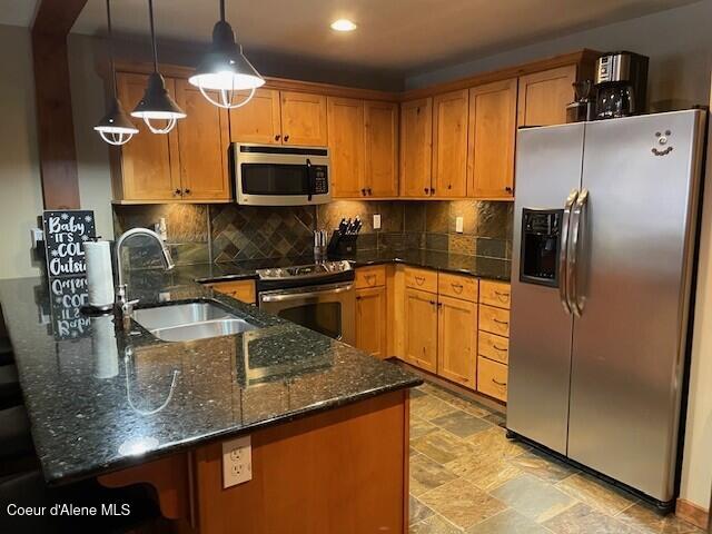 kitchen with backsplash, stainless steel appliances, sink, decorative light fixtures, and dark stone countertops