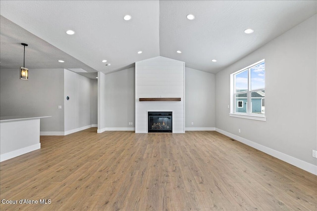 unfurnished living room with a textured ceiling, light hardwood / wood-style floors, a fireplace, and vaulted ceiling