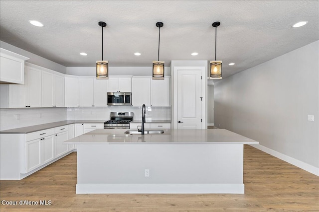 kitchen featuring a center island with sink, white cabinets, sink, hanging light fixtures, and stainless steel appliances