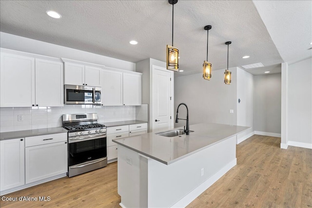 kitchen with appliances with stainless steel finishes, sink, white cabinets, hanging light fixtures, and an island with sink