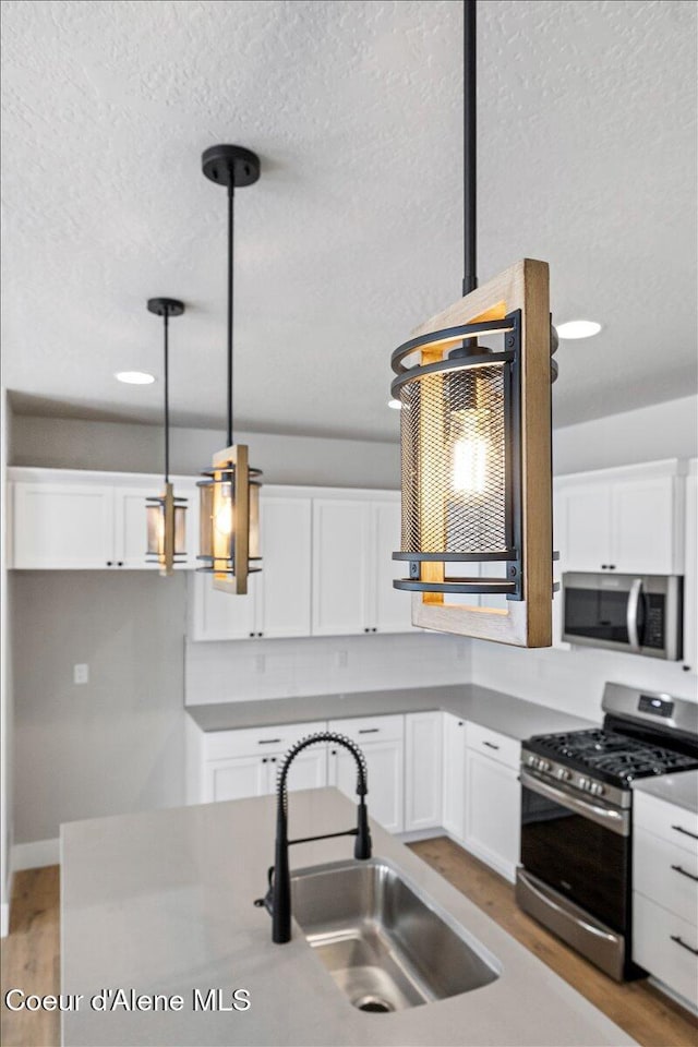 kitchen with appliances with stainless steel finishes, light wood-type flooring, sink, decorative light fixtures, and white cabinetry