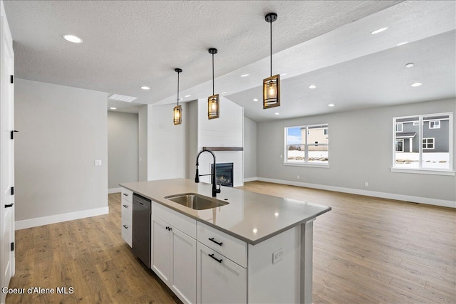 kitchen with a kitchen island with sink, sink, hanging light fixtures, stainless steel dishwasher, and white cabinetry