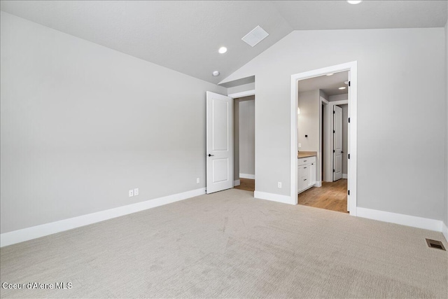 unfurnished bedroom with ensuite bathroom, light colored carpet, and lofted ceiling